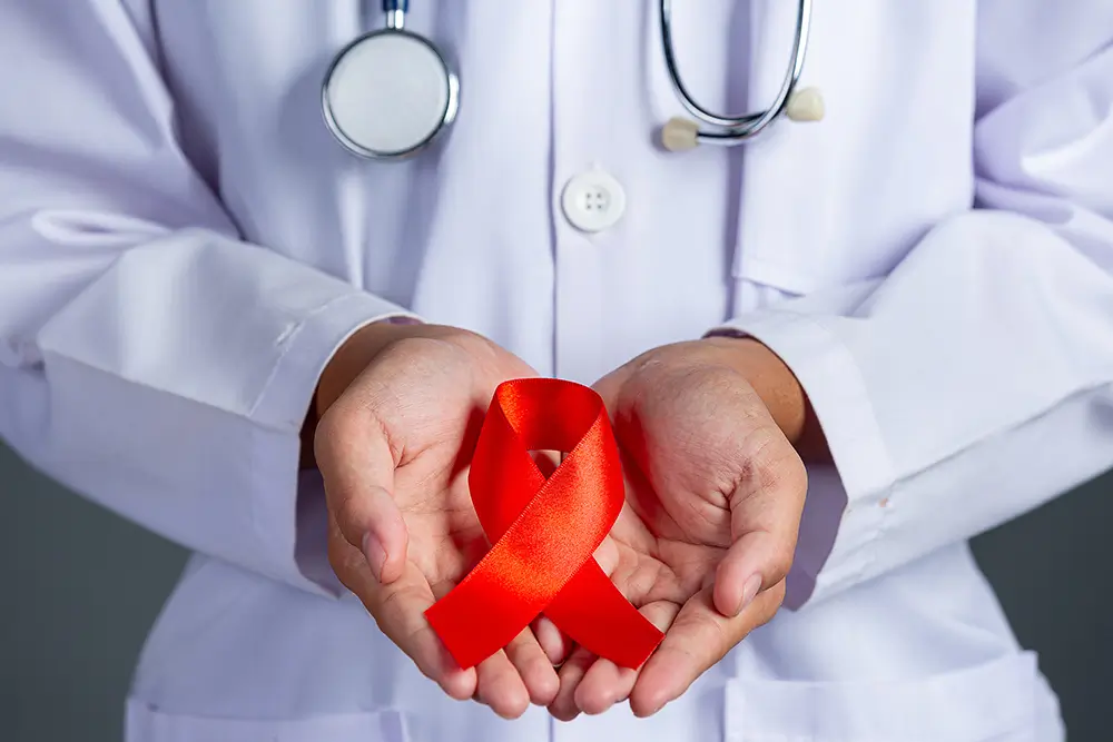 Doctor in white coat holding red HIV awareness ribbon