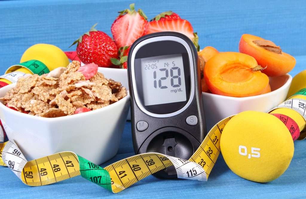 Glucose meter showing blood sugar level surrounded by healthy foods and fitness equipment