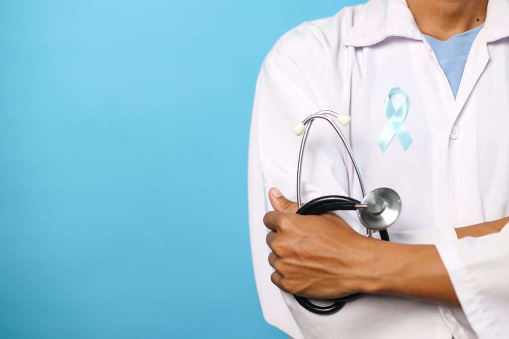 Doctor in white coat holding stethoscope with light blue awareness ribbon