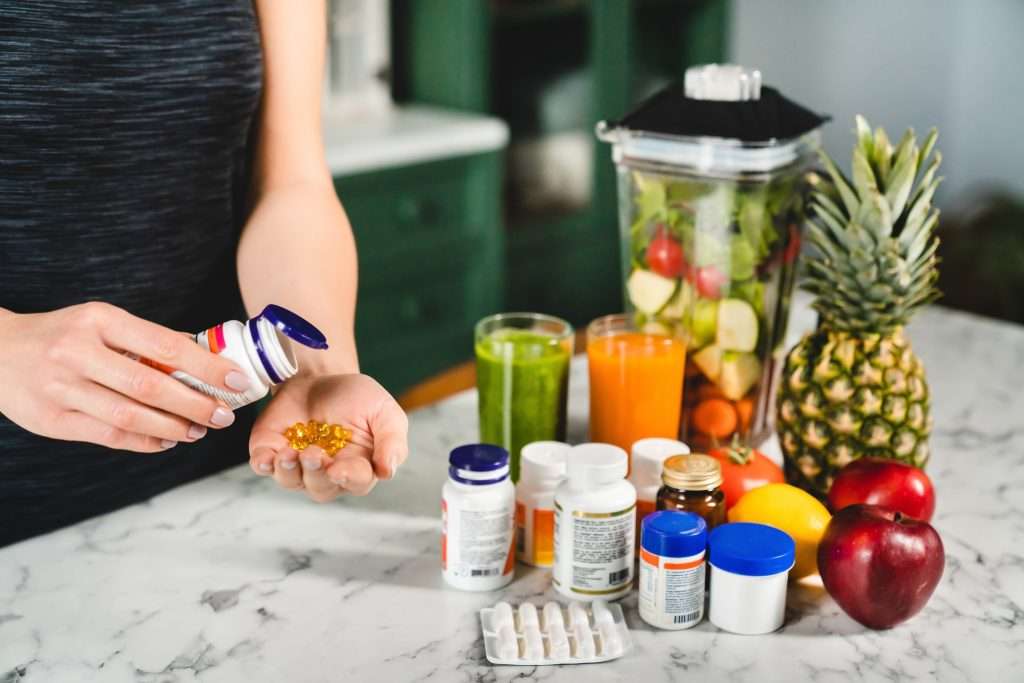 Woman holding vitamin supplements with fresh fruits and juices on table