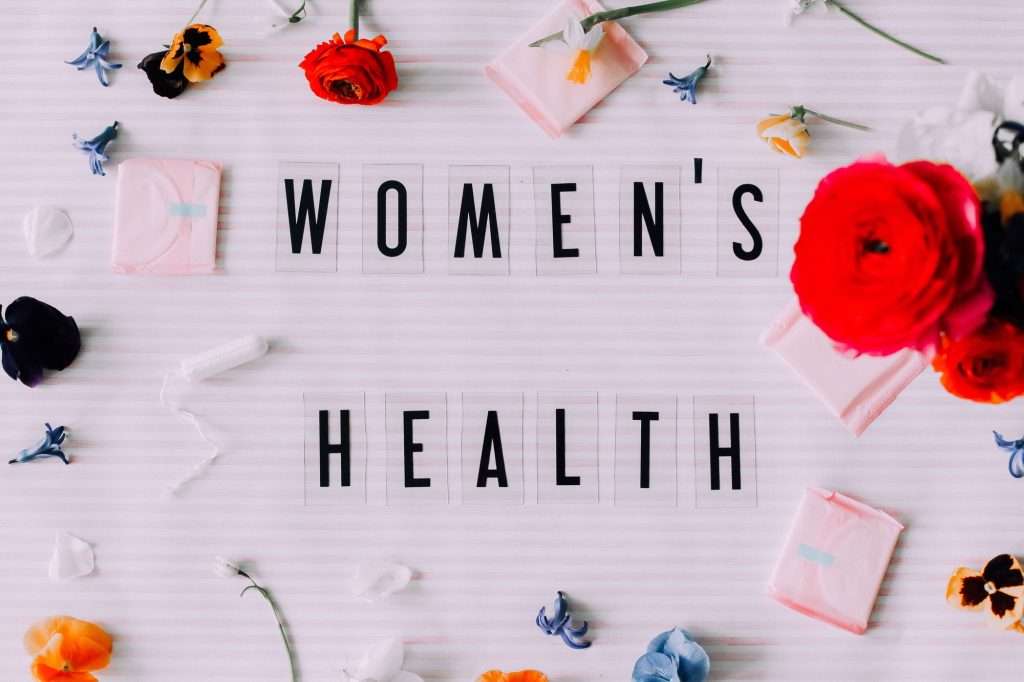 Women's health text surrounded by flowers and pink wellness items on white background