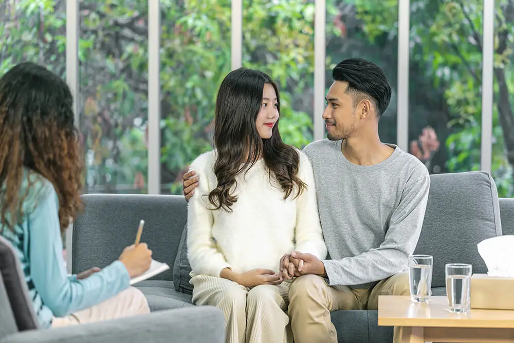 Couples therapy session with counselor taking notes while couple sits together on couch